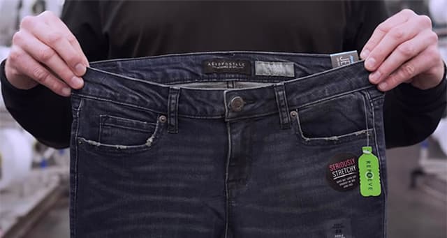 Person's hands hold up a pair of denim jeans made out of reycled materials