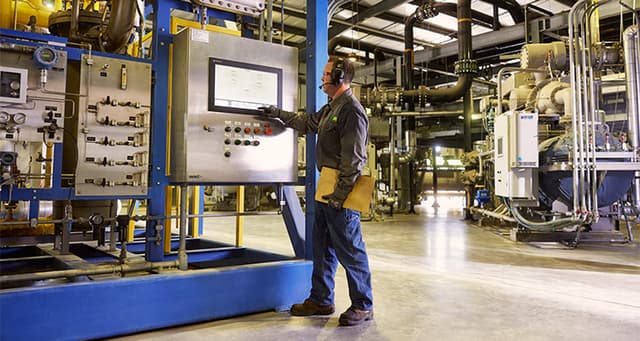 Tech pressing buttons on a large control panel for interior machinery at a WM renewable natural gas facility