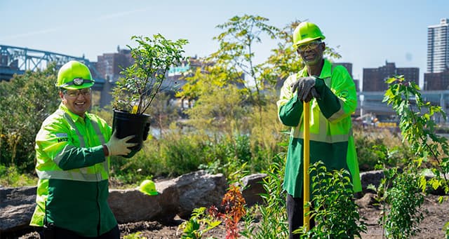 Two WM employees in bright green safety gear and hardhats take a break from planting in an urban garden on Community Day