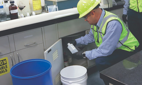 A WM employee wearing a hard had and a reflective vest in a lab assessing waste for proper and safe disposal