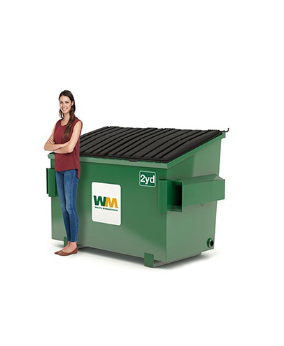 Une femme se tient à côté d'une benne de 2 verges de Waste Management.