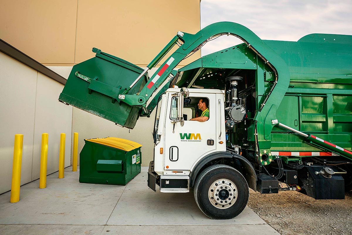 A Waste Management dumpster being collected by a truck. 