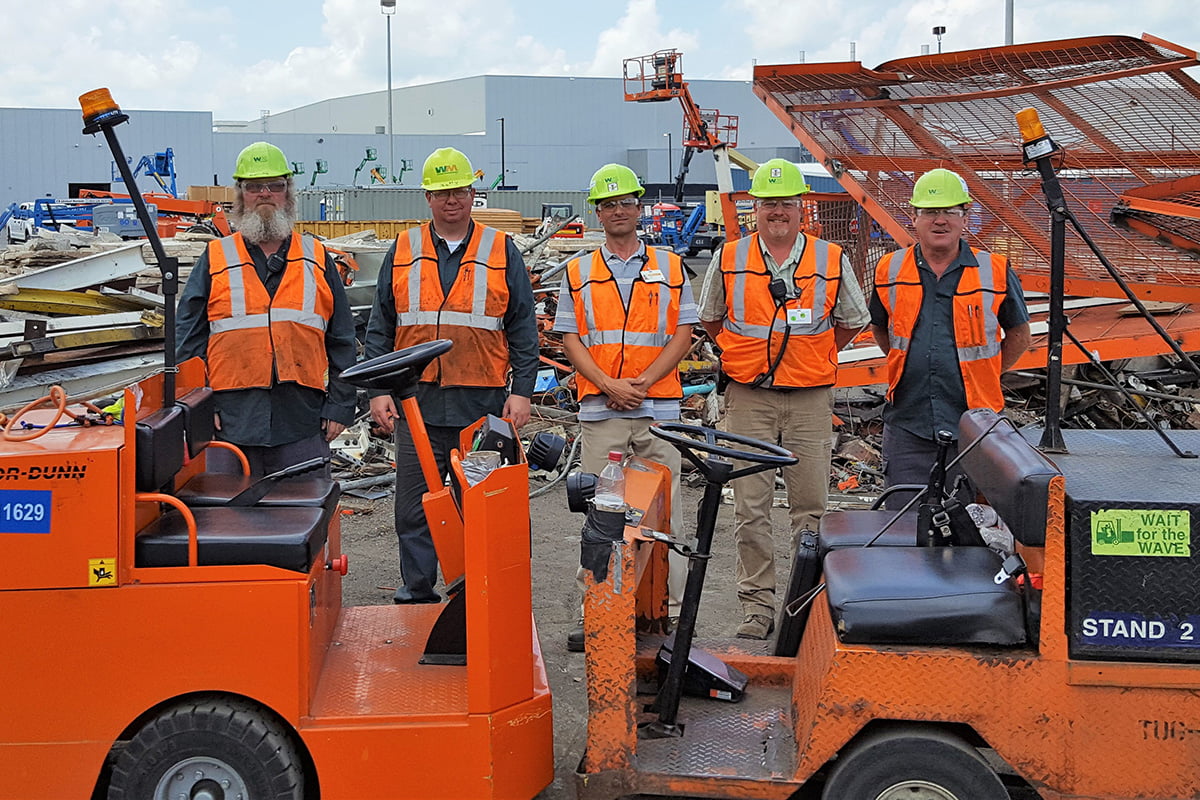Group of technicians standing for a photo in orange safety vests outside a WM Environmental Solutions site