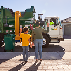 Two children wave at a WM driver collecting residential trash and recycling.
