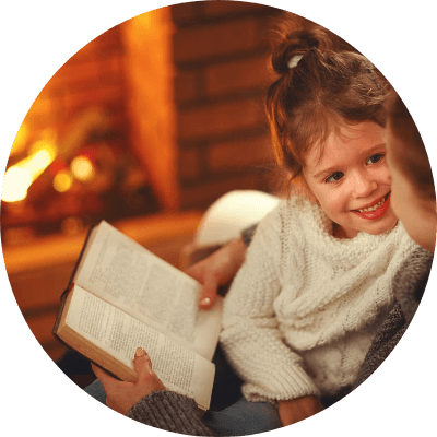 A little girl and her mother sitting in front of a fireplace reading a book.