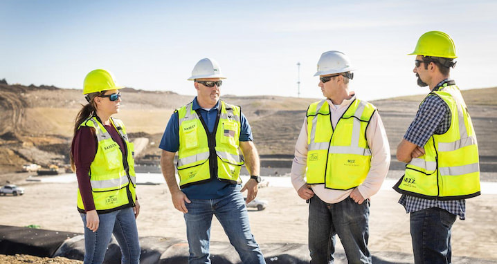 Four WM technicians talk in front of a WM landfill that's under construction for renewable energy collection.
