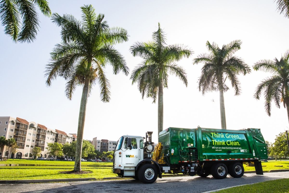 A WM garbage truck passes up a row of palm trees on its commercial trash pickup route in Seffner, Florida.