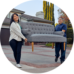 Two people carry a gray couch to curb for bulk waste pickup