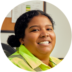 Closeup of WM employee with safety yellow top smiling to camera while sitting at desk in office